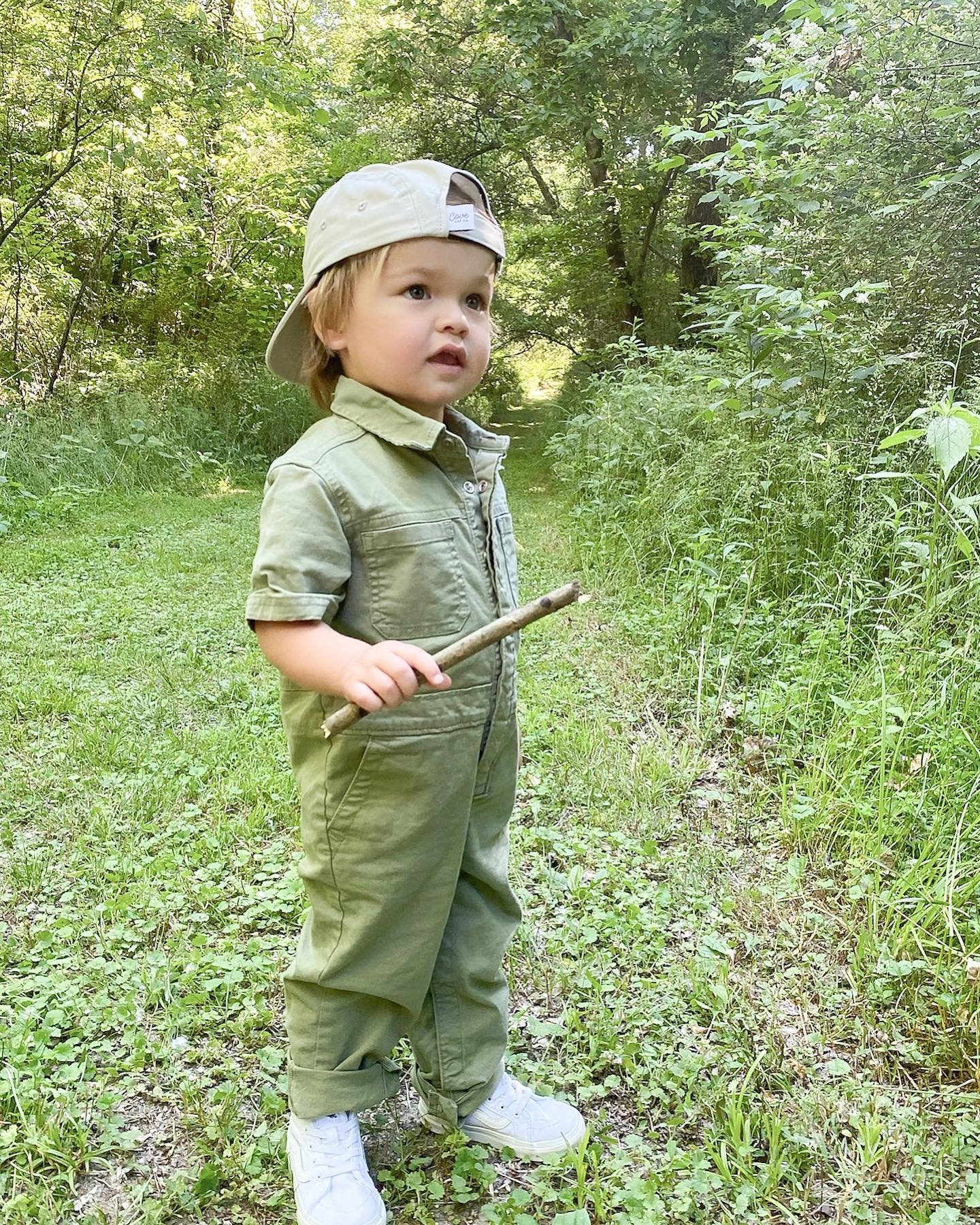 Toddler wearing a grey / beige sun hat backwards while exploring in the forest. Hat is a minimalist five-panel design, made in Canada out of organic cotton.