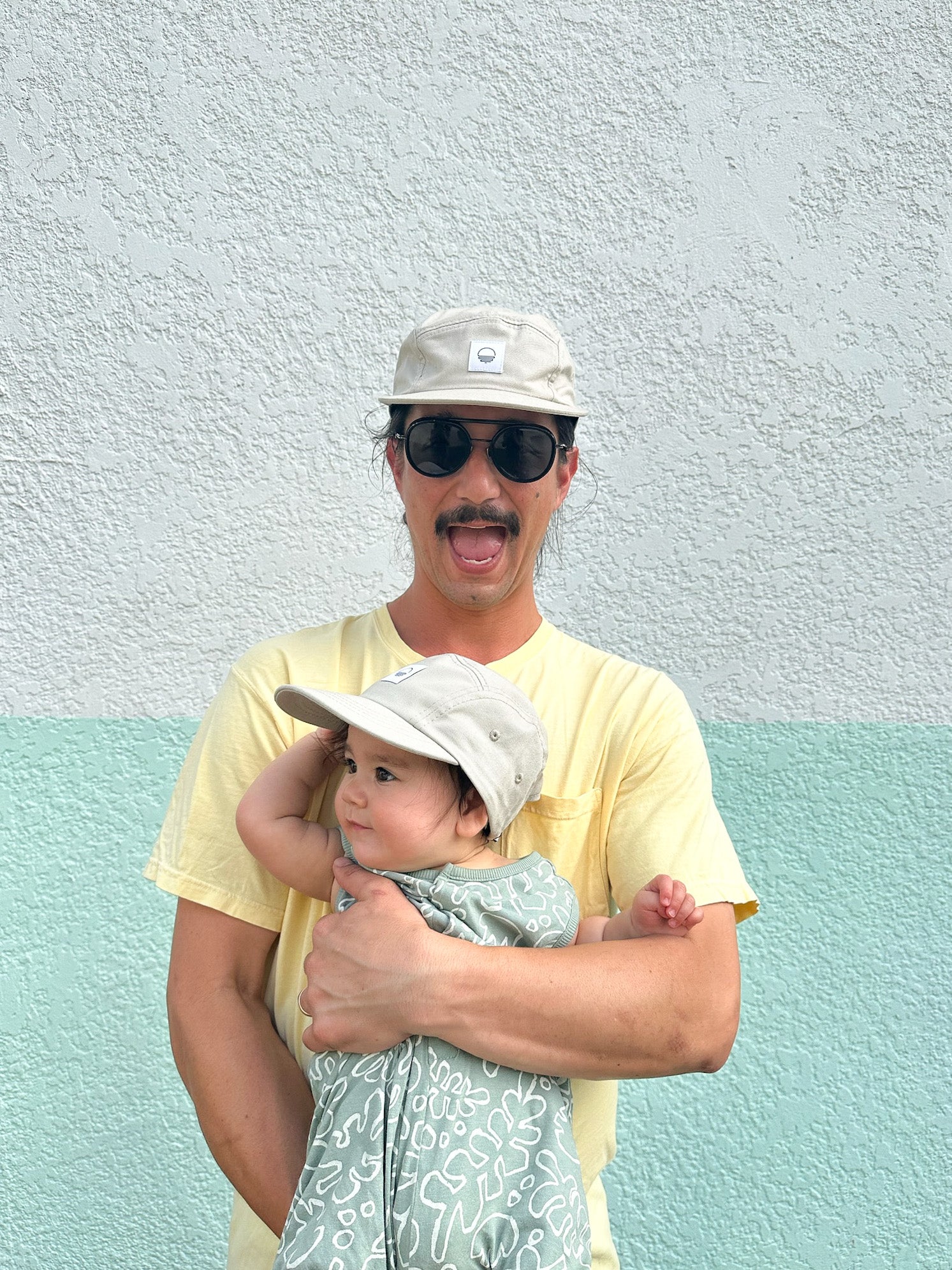 Father and daughter wearing matching grey five-panel sun hats. Child is in a toddler size hat, father is wearing an adult size. Minimalist design, made in Canada out of organic cotton.