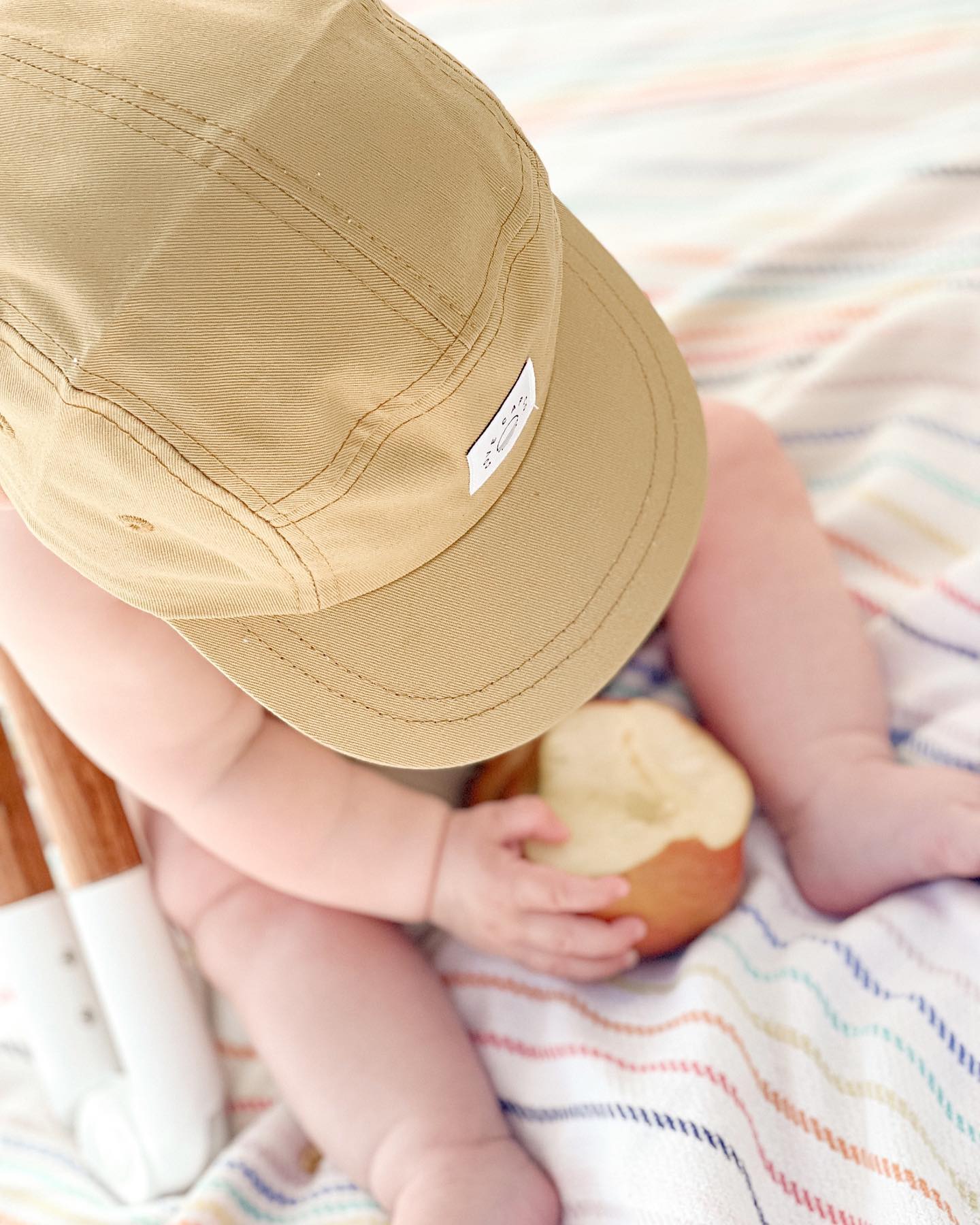 Toddler wearing a yellow sun hat while sitting on a blanket under a beach umbrella. Mustard yellow hat is a minimalist five-panel design, made in Canada out of organic cotton. 