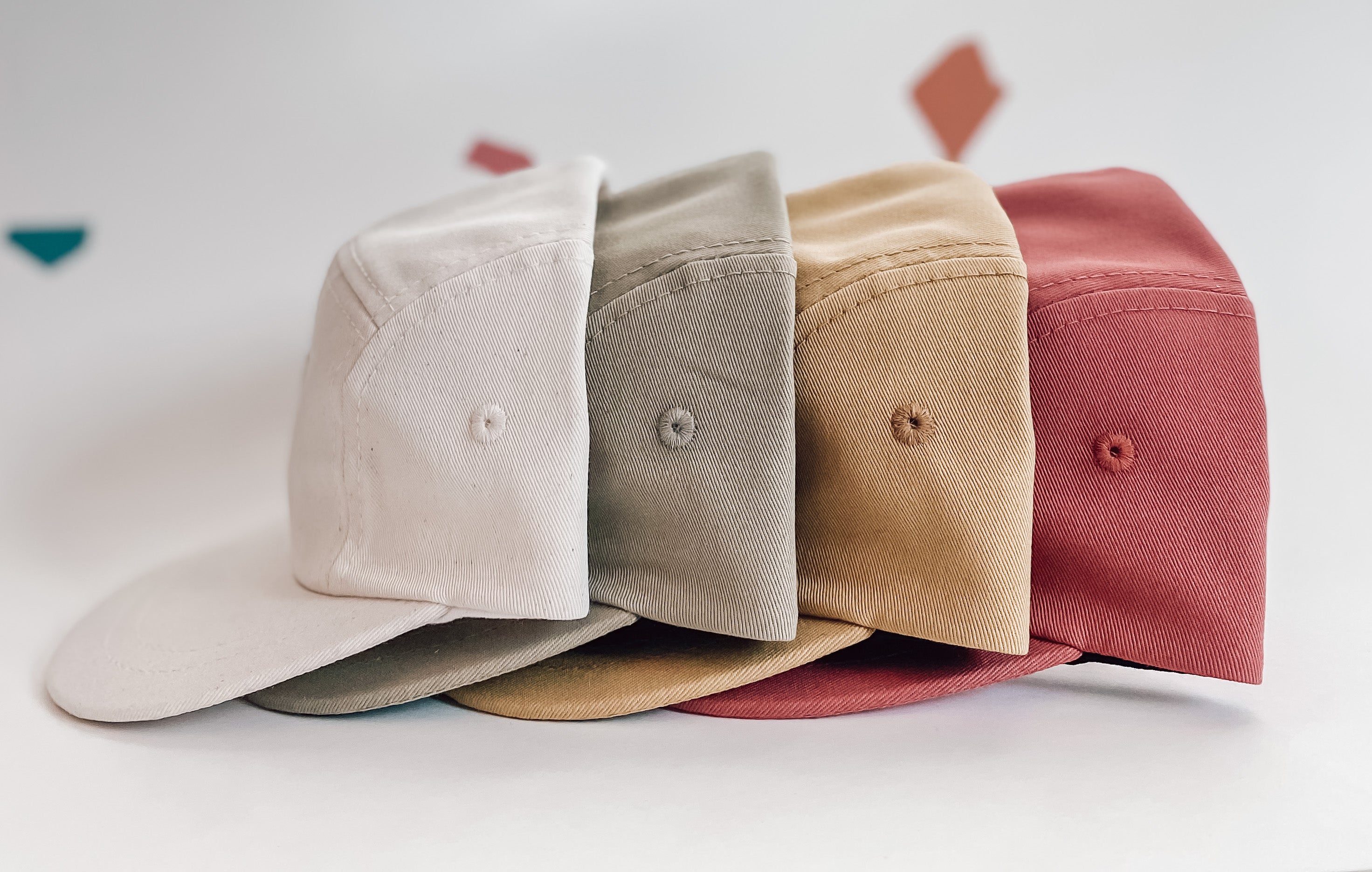 A row of four toddler / kids sun hats. Colours include white / off white, khaki green, mustard yellow, and a pink / red. Hats are a minimalist five-panel design, made in Canada out of organic cotton. Hats have an adjustable soft velcro closure. 